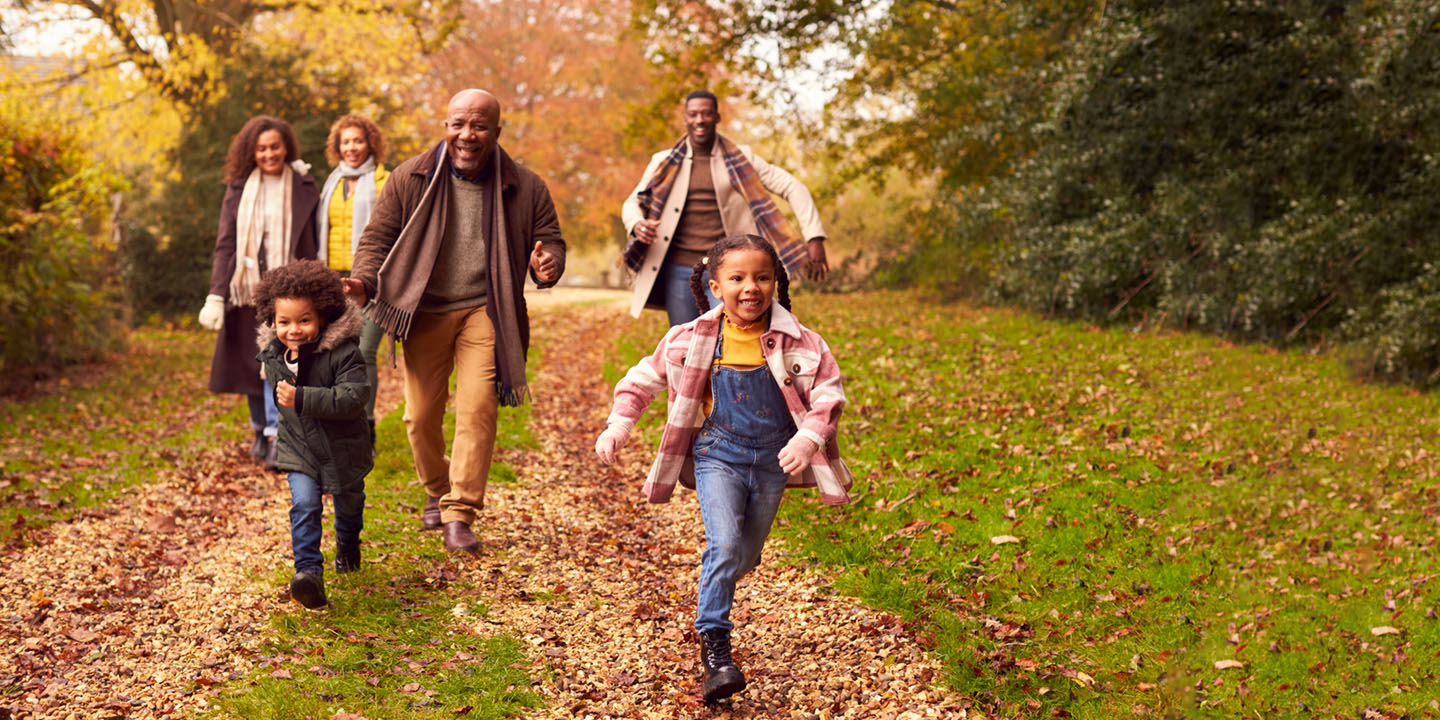 Family in park running though autumn leaves