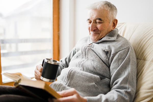 Man on sofa reading a book with a drink 