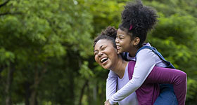 Mother carrying a child on her back in a park 