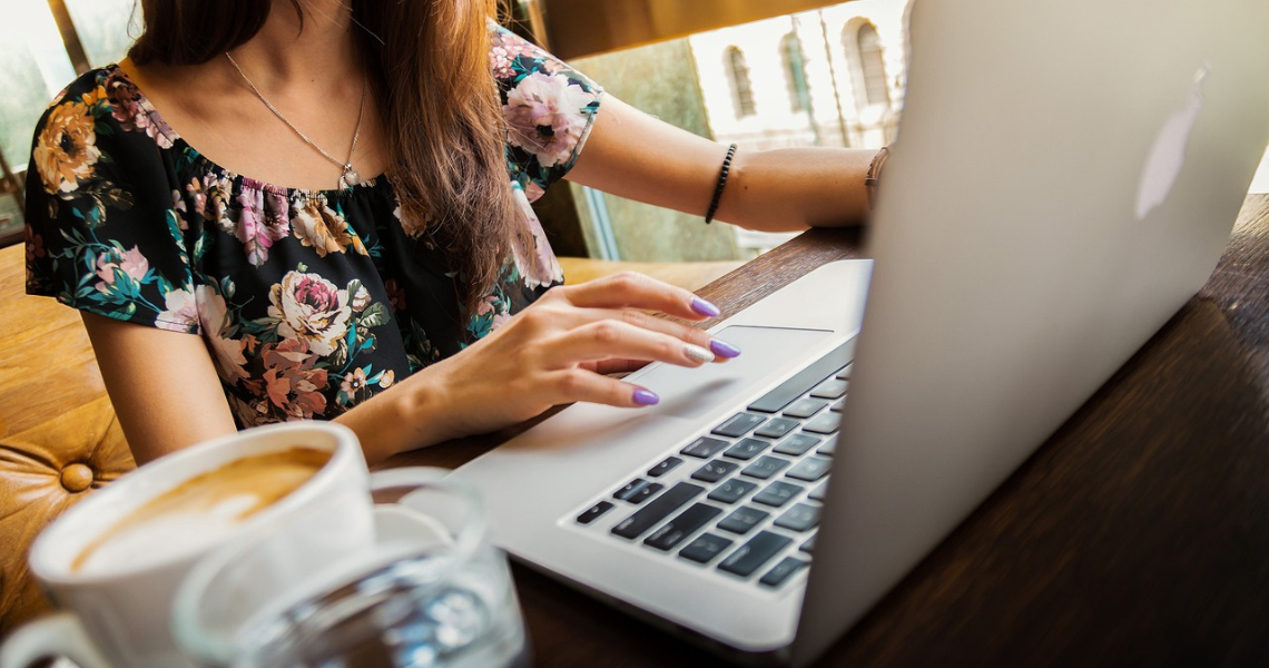 Woman typing on a laptop with a coffee next to her