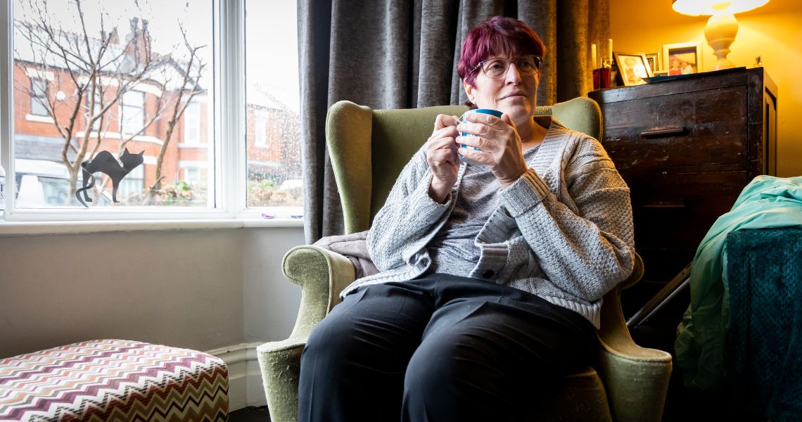 Person having a cup of tea, wearing a woolly jumper, by a window at home