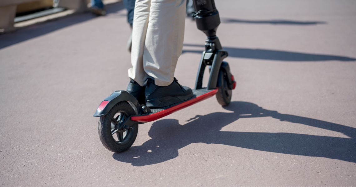 An e-scooter being ridden on a concrete path.