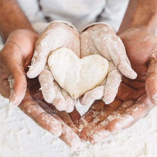 A mans hands which are cupped together with a child's hands resting on the mans hands, holding a heart shaped biscuit