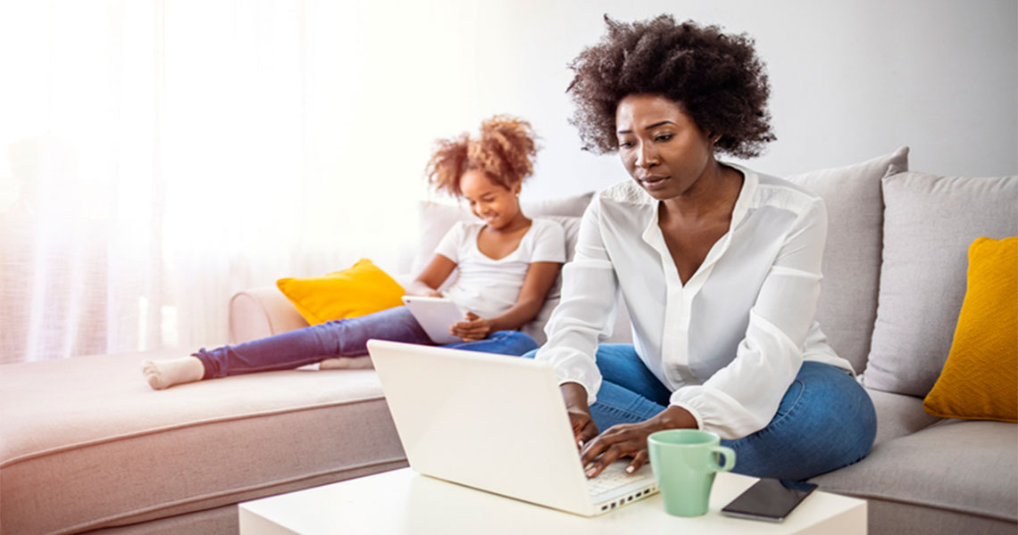 woman using a laptop and girl in the background on a tablet