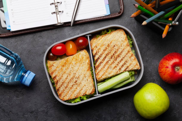 lunch box containing a sandwich on a desk with paper and pens