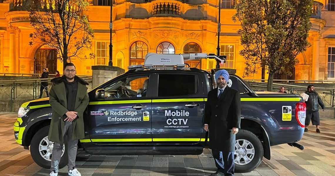 two men stand in front of a land rover, which is a very dark blue with yellow visibility stripes