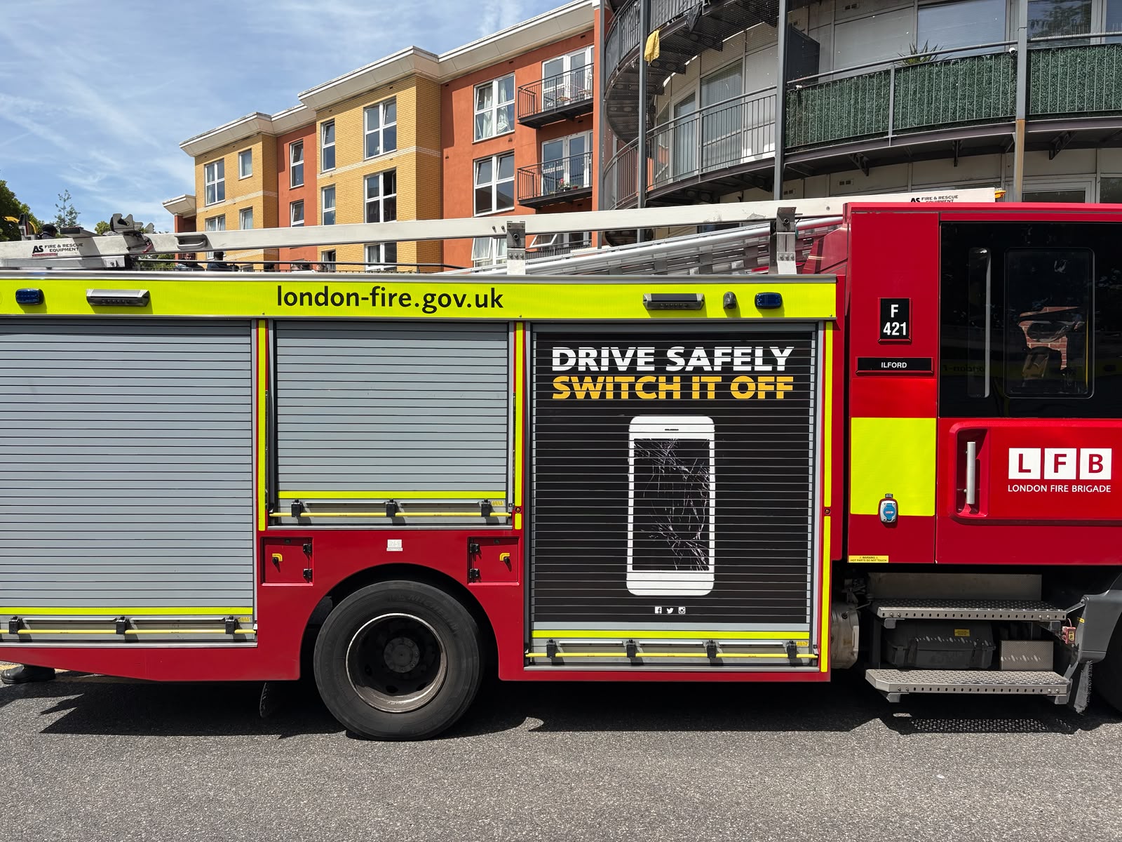 A London Fire Brigade fire engine is parked on a residential street in front of a modern apartment building