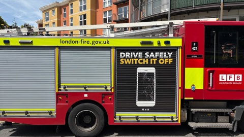 A London Fire Brigade fire engine is parked on a residential street in front of a modern apartment building