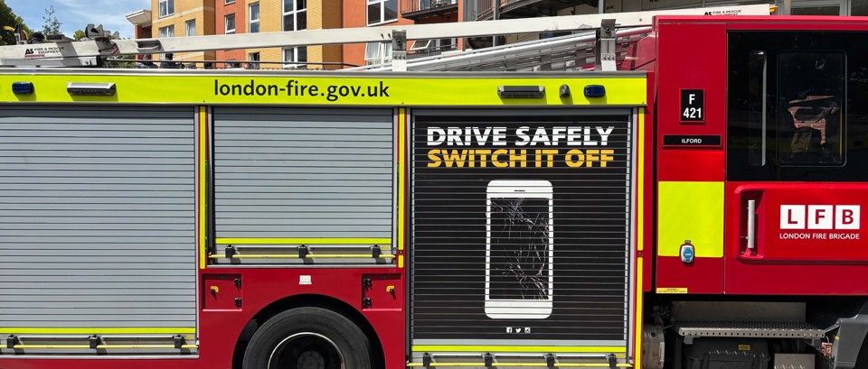 A London Fire Brigade fire engine is parked on a residential street in front of a modern apartment building