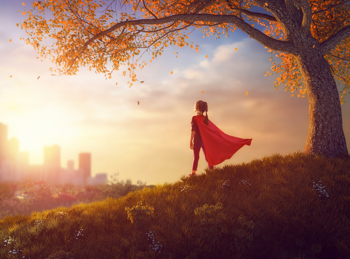 Young girl, wearing a cape, standing on a hill, looking out at the city ahead