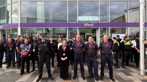 A diverse group of people stands together in front of a large building, smiling and engaging with one another.