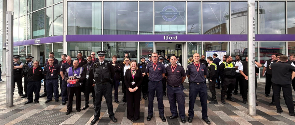 A diverse group of people stands together in front of a large building, smiling and engaging with one another.
