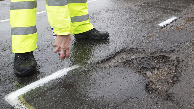 Highways operative spraying white marker around pothole that needs to be repaired image